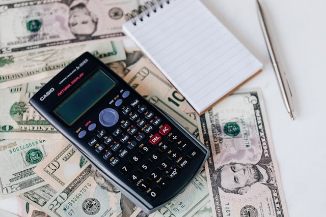 A calculator, notepad and pen next to money